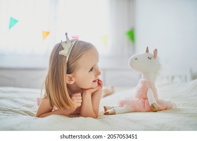 Adorable little girl in pink dress and golden crown dressed as princess playing with unicorn. Kid having fun with soft toy. Child playing with stuffed toy - Shutterstock ID 2057053451