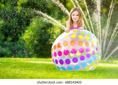 Adorable Little Girl Playing With Inflatable Beach Ball In A Backyard On Sunny Summer Day. Cute Child Having Fun With Water Outdoors. Funny Summer Games For Kids.