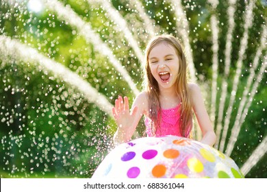 Adorable Little Girl Playing With Inflatable Beach Ball In A Backyard On Sunny Summer Day. Cute Child Having Fun With Water Outdoors. Funny Summer Games For Kids.