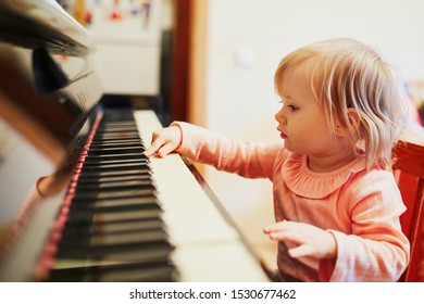 Adorable little girl playing piano. Toddler having fun while learning how to play music. Musical education for small kids