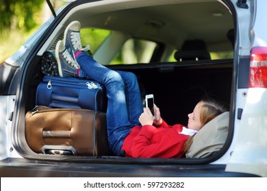 Adorable Little Girl Ready To Go On Vacations With Her Parents. Kid Playing With Her Phone In A Car. Traveling By Car With Kids. 