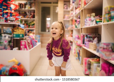 Adorable Little Girl Shopping For Toys. Cute Female In Toy Store. Happy Young Girl Selecting Toy