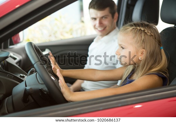 Adorable little girl sitting in the driver place\
in a car with her father driving drive license travel travelling\
tourism children kids family childhood enjoyment emotions bonding\
activity