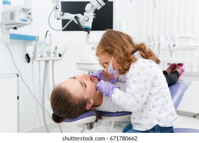 Adorable little girl sitting and making an examination of woman doctor lying on dentist chair in hospital. Dentist and child in cabinet. Dentist office. Little girl in the dentists office