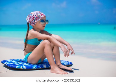 Adorable little girl sitting on surfboard at the seashore