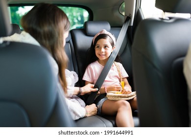 Adorable little girl smiling and looking at her mom while putting their safety seat belt on in the car before starting a family road trip