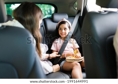 Adorable little girl smiling and looking at her mom while putting their safety seat belt on in the car before starting a family road trip