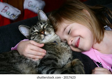 Adorable Little Girl Snuggling With Her Pet Cat.  Christmas Stockings Hanging In The Background.