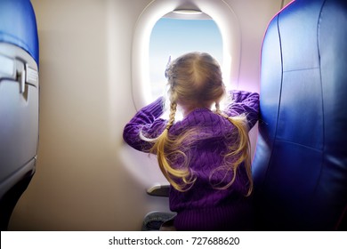 Adorable Little Girl Traveling By An Airplane. Child Sitting By Aircraft Window And Looking Outside. Traveling With Kids Abroad.