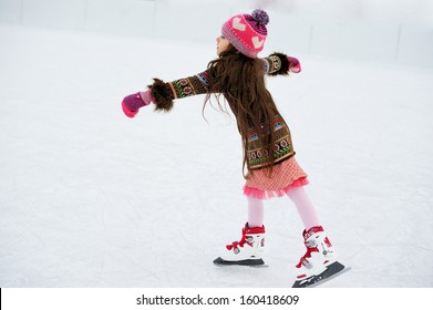 Adorable Little Girl In Winter Clothes And Bobble Hat Skating On Ice Rink