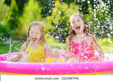 Adorable Little Girls Playing In Inflatable Baby Pool. Happy Kids Splashing In Colorful Garden Play Center On Hot Summer Day. Summer Activities For Kids.