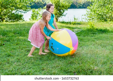 Adorable Little Girls Playing With Toy Ball Garden Sprinkler With Water Splashes In A Backyard On Sunny Summer Day. Cute Child Having Fun With Water Outdoors. Funny Summer Games For Kids