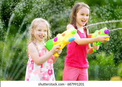 Adorable Little Girls Playing With Water Guns On Hot Summer Day. Cute Children Having Fun With Water Outdoors. Funny Summer Games For Kids.