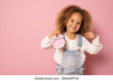 Adorable Little Kid Girl In Casual Clothing Smiling And Holding Alarm Clock Isolated Over Pink Background