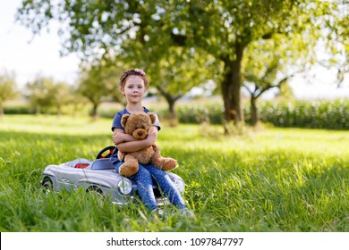 Adorable Little Kid Girl Sitting On Big Vintage Old Toy Car And Having Fun With Playing With Big Plush Toy Bear,