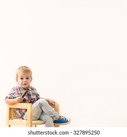 Adorable Little Kid Sitting On Chair And Holding Candy In One Hand. Studio Shot.