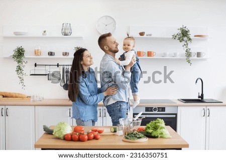 Adorable little lady in denim clothes laughing with caring parents while dad holding baby daughter in arms. Happy spouses and kid building lifelong memories while upholding family culinary tradition.