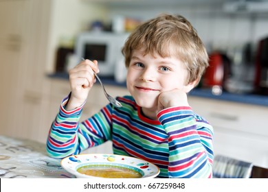 Adorable little school boy eating vegetable soup indoor. Blond child in domestic kitchen or in school canteen. Cute kid and healthy food, organic vegan soup with potato, tomato and vegetables - Powered by Shutterstock