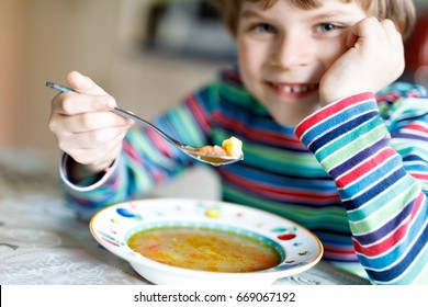 Adorable Little School Boy Eating Vegetable Soup Indoor. Blond Child In Domestic Kitchen Or In School Canteen. Selective Focus On Hand Of Kid.