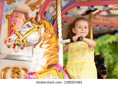 Adorable little toddler girl on carousel horse. child on attraction. kid entertainment. Happy healthy baby having fun outdoor on sunny day. Family weekend, vacations, holiday. 