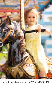 Adorable Little Toddler Girl On Carousel Horse. Child On Attraction. Kid Entertainment. Happy Healthy Baby Having Fun Outdoor On Sunny Day. Family Weekend, Vacations, Holiday. Vertical