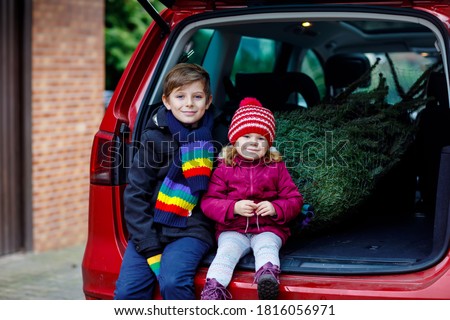 Adorable little toddler girl and school kid boy with Christmas tree inside of family car. Happy healthy children in winter fashion clothes buying big Xmas tree for traditional celebration.