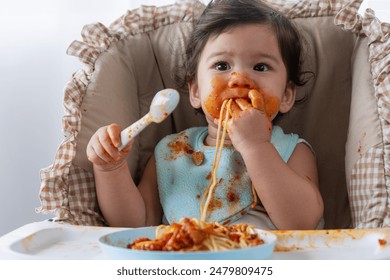 Adorable messy little child girl hungry use hand eating spaghetti sitting in high-powered chair at home. Toddler child with tomato sauce making mess face looking at food. Self-feeding concept - Powered by Shutterstock