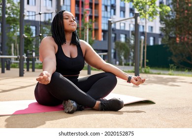 Adorable mixed race woman in sport clothes sitting in lotus position yoga mat and with namaste hands. Young black woman keeping eyes closed while meditating on fresh air, breathing correctly - Powered by Shutterstock