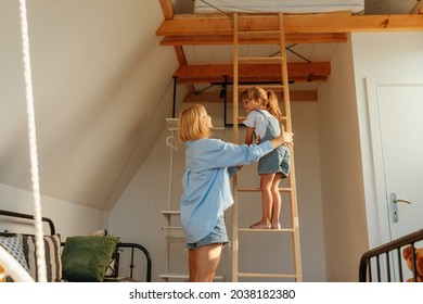 Adorable Mom And Daughter Having Fun At Home. Mother Helping Her Daughter To Climb Up The Ladder At Home