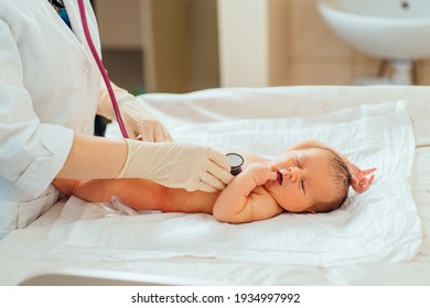 Adorable Newborn Baby Boy In Diaper Check Up Examines By Pediatrician Doctor. Female Doctor Hand Using Stethoscope Examining Little Cute Baby Infant Heart, Lung In Clinic. Health Care Concept.