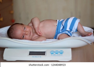 Adorable newborn baby boy lying on the baby weight scale at home, healthy growth and family care