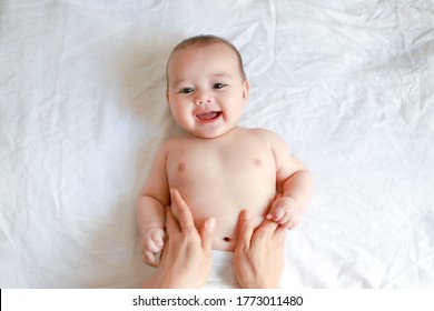 Adorable Newborn Baby Boy With Smiling Face Top View Relaxing Time Doing Belly Massage By His Mother. Mixed Race Asian-German Infant Massaging And Laughing.