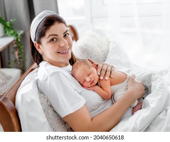 Adorable Newborn Baby Sleeping On Chest Of Young Mother. Portrait Of Beautiful Woman Holding Her Infant, Looking At The Camera And Smiling. Mom With Child At Home With Daylight