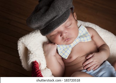Adorable newborn wearing a bow-tie and hat fast asleep in a red basket.