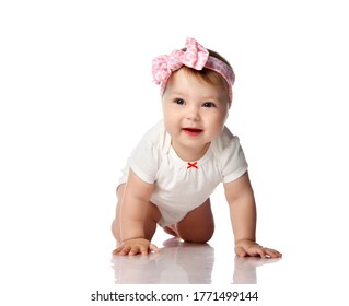 Adorable positive little baby girl in white cotton body, hair bow decoration and barefoot creeping on floor, smiling and looking aside over white background. Happy childhood concept - Powered by Shutterstock