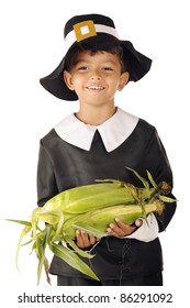 An adorable preschool boy wearing Pilgrim clothes carrying an armload of fresh corn on the cob.