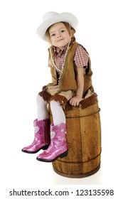 An adorable preschool cowgirl sitting pretty on an old barrel.  On a white background.
