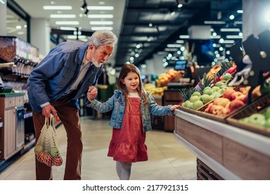 Adorable preschool girl holding hand of her grandfather who carrying mesh bag. They are in supermarket and buying organic fruit together - Powered by Shutterstock