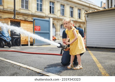 Adorable preschooler girl acting like a fireman holding firehose nozzle and splashing water
