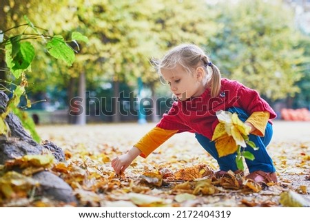 Adorable preschooler girl enjoying nice and sunny autumn day outdoors. Happy child gathering autumn leaves in Paris, France. Outdoor fall activities for kids
