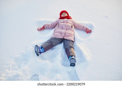 Adorable Preschooler Girl Making Snow Angel In Beautiful Winter Park On A Snowy Cold Winter Day. Cute Child Playing In Snow. Winter Activities For Family With Kids