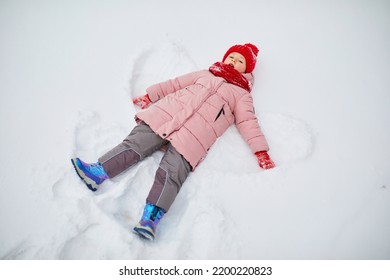 Adorable Preschooler Girl Making Snow Angel In Beautiful Winter Park On A Snowy Cold Winter Day. Cute Child Playing In Snow. Winter Activities For Family With Kids