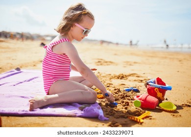 Adorable preschooler girl playing on the sand beach at Atlantic coast of Brittany, France. Small child enjoying vacation by the sea or ocean. Travelling with kids - Powered by Shutterstock