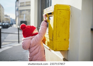 Adorable preschooler girl putting letter in yellow post box on a street of Paris, France - Shutterstock ID 2337157857