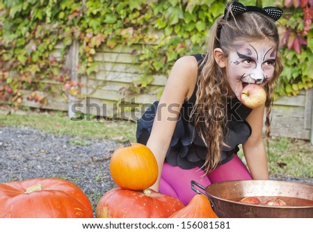 Adorable, pretty, young girl dressed as a black cat, apple bobbing for Halloween