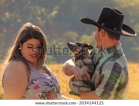 Adorable romantic photo of a beautiful young couple in a field with their dog. Cowboy and wife on a meadow in the countryside during sunset. Blurred background 