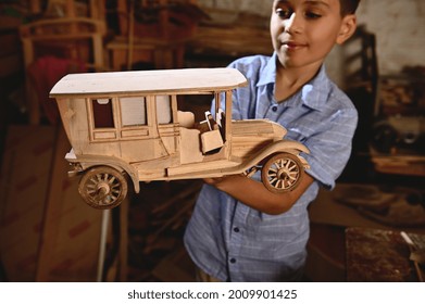 Adorable Schoolboy Holding A Wooden Model Of Handmade Car. Carpentry, Hobby, Wood Carving Industry. Focus On Wooden Car