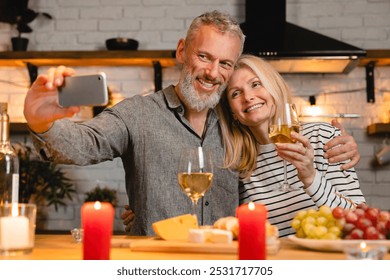 Adorable senior couple taking selfie on the phone during romantic date in the kitchen. Special event celebration. Spouses on videocall on Valentine`s Day. Dating concept - Powered by Shutterstock