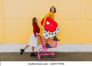 Adorable sisters having fun during shopping. Two glamorous girls posing with heart symbol.