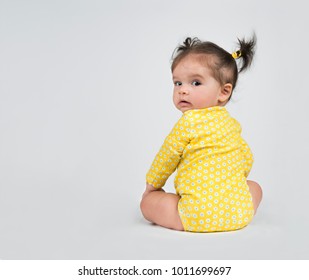 Adorable, Sitting, Baby Girl In Yellow Onesie, On White Background,  Looking Back Over Her Shoulder